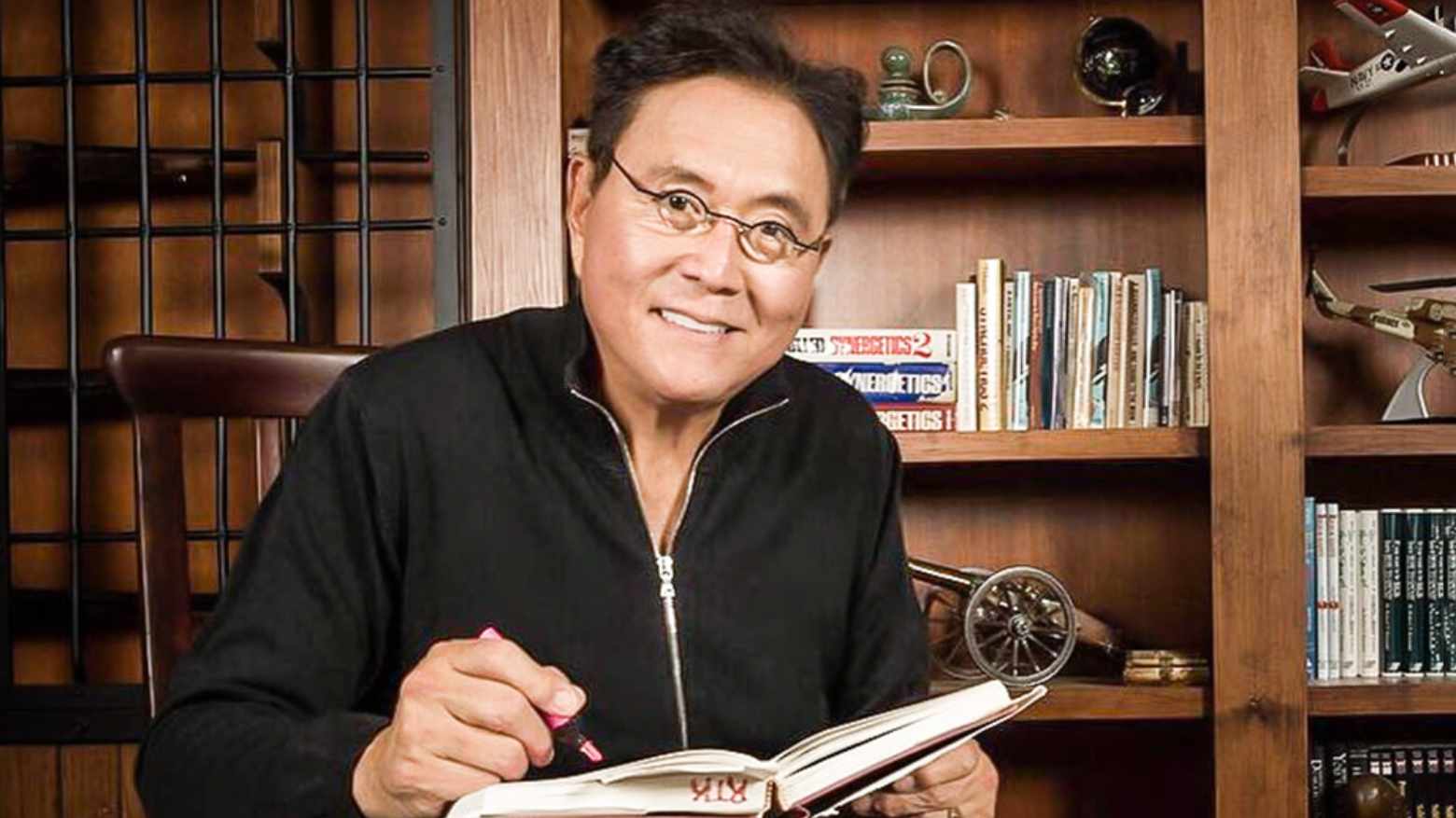 Robert Kiyosaki, autor de Pai Rico Pai Pobre, apontando para gráfico de investimentos com foco em Bitcoin, ouro e prata para crise de 2025.