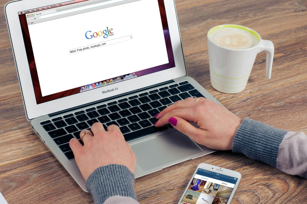 Google fora do ar? Entenda a instabilidade nos serviços em 2025 2 Mãos digitando no MacBook Air com a pesquisa do Google aberta e café por perto.