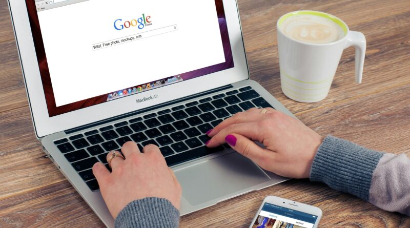 Mãos digitando no MacBook Air com a pesquisa do Google aberta e café por perto.