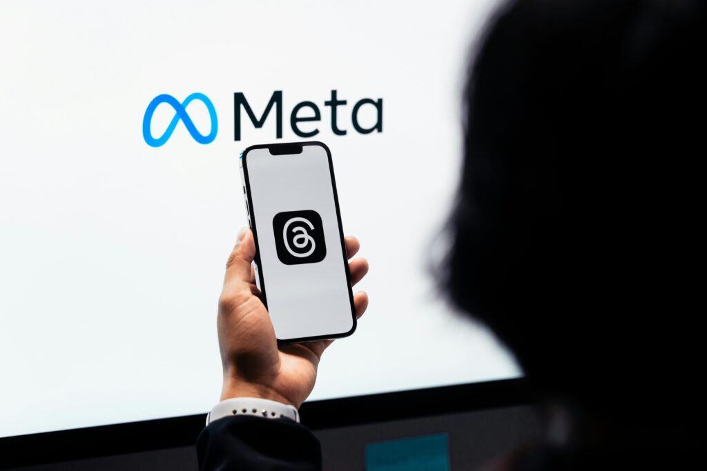 Meta AI app: Um pesadelo de privacidade exposto 3 Mãos segurando um smartphone com o logotipo da Meta Threads na tela e a marca Meta ao fundo.