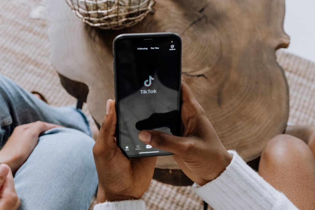 Close-up de mãos segurando um smartphone exibindo a interface do aplicativo TikTok em uma superfície de madeira.