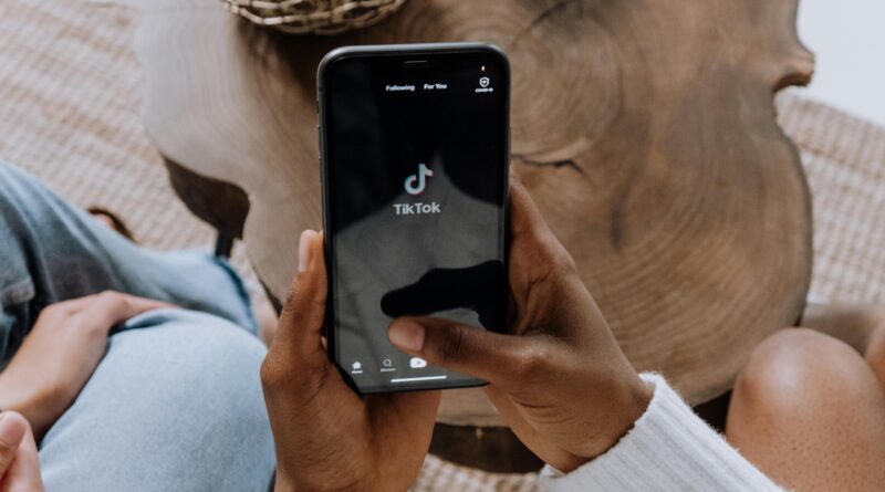 Close-up de mãos segurando um smartphone exibindo a interface do aplicativo TikTok em uma superfície de madeira.