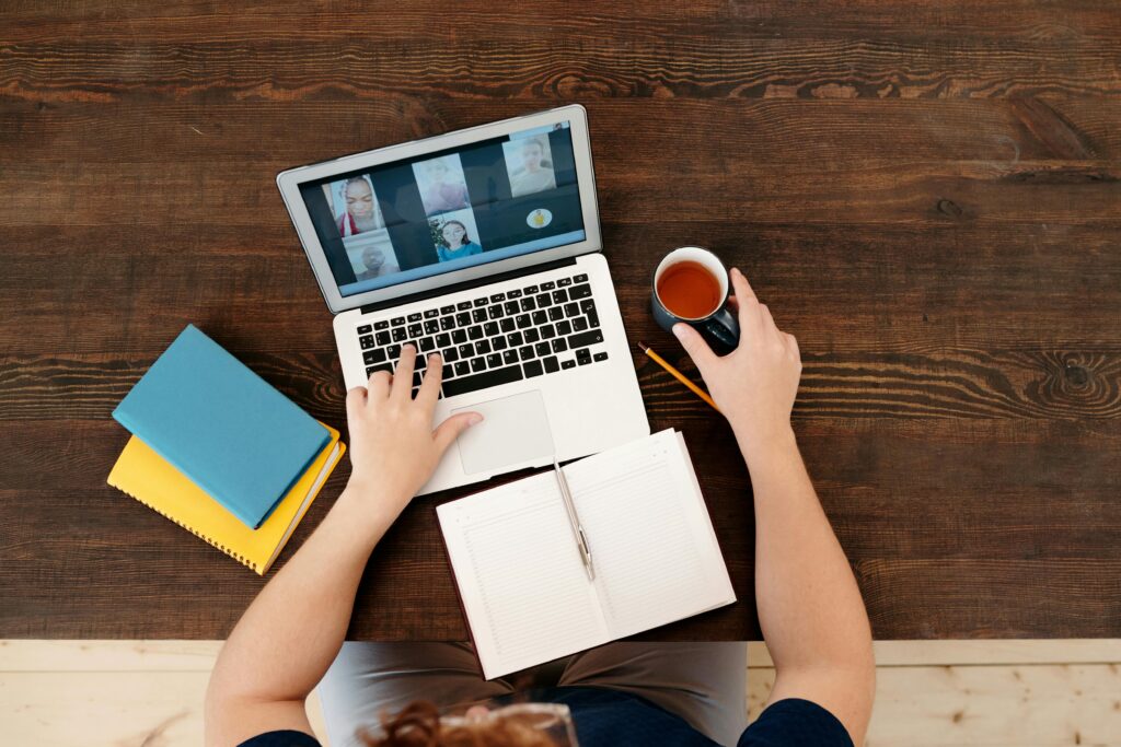 Tactiq AI: como usar grátis para transcrever reuniões online 3 Uma pessoa participando de uma reunião virtual em um laptop com café e cadernos em uma mesa de madeira.