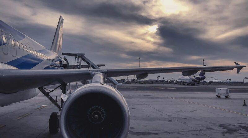 Um avião de passageiros está estacionado na pista ao pôr do sol, com outra aeronave ao fundo.