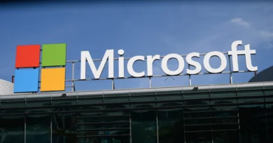 Fachada de um escritório da Microsoft; logotipo iluminado em azul sob céu nublado