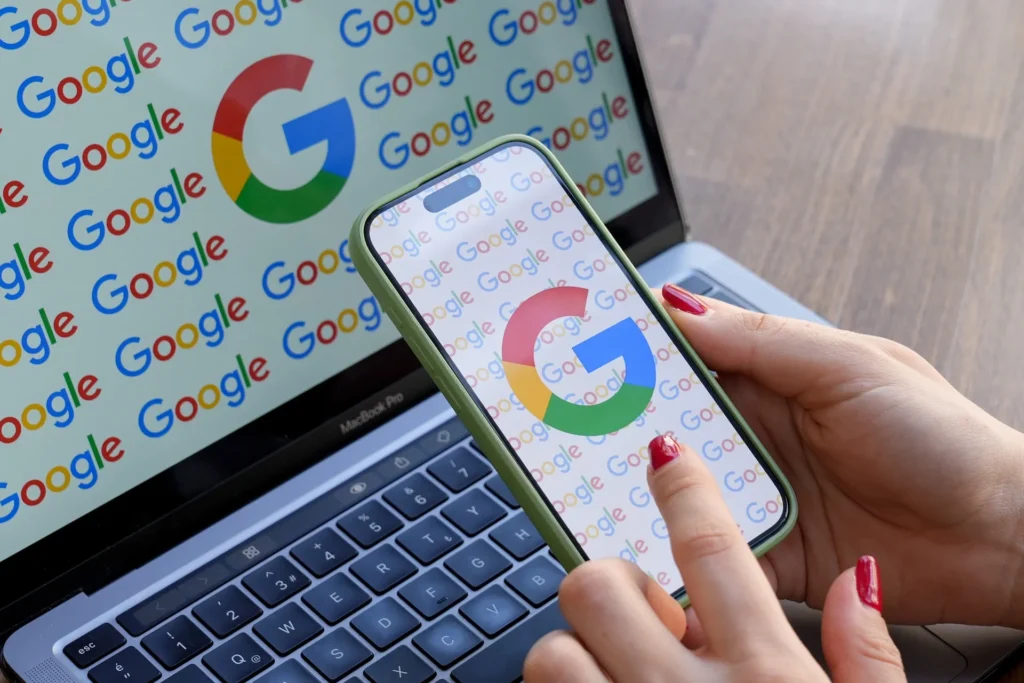 Google lança Fontes Preferidas para personalizar notícias 2 Mulher olha para celular exibindo o logo do Google, com logo do Google em monitor ao fundo; lançamento do Fontes Preferidas em agosto de 2025 nos EUA e Índia.