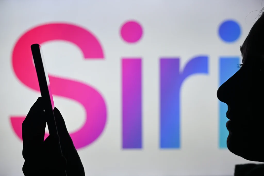 Mulher segura smartphone na frente do logo da Siri em uma tela – Novo Siri da Apple para controle por voz.