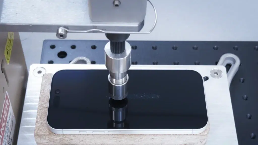 Tela do iPhone sendo testada contra riscos utilizando material abrasivo; resultado sem danos visíveis