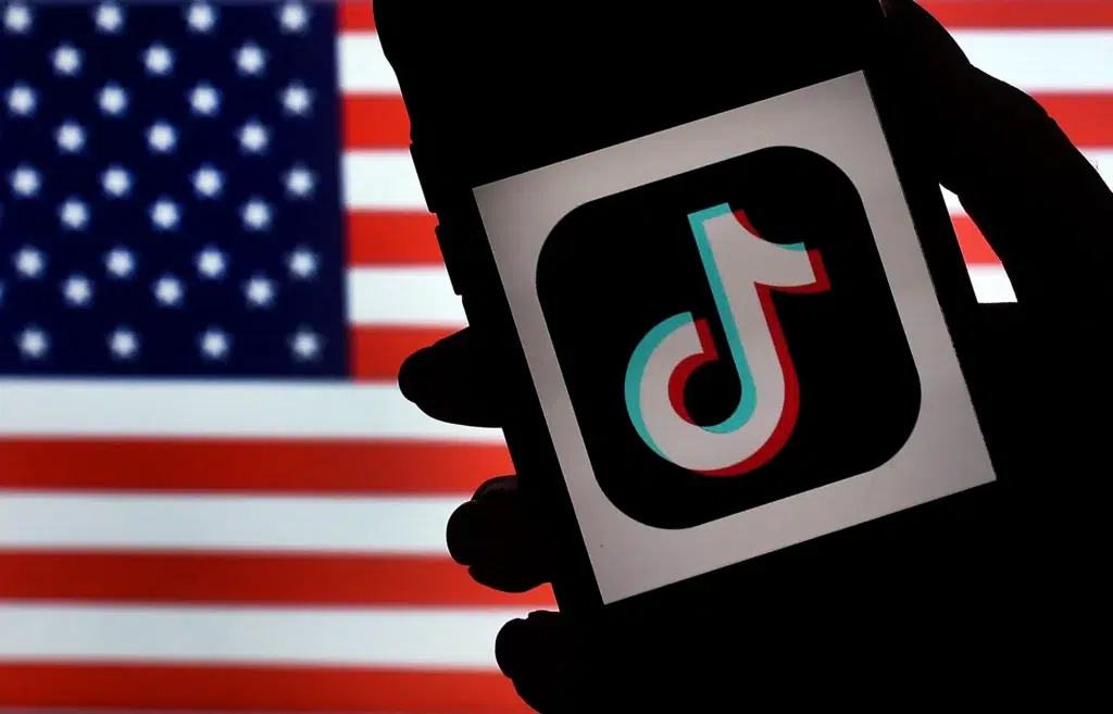 Acordo do TikTok nos EUA: imagem do app em iPhone sobre bandeira dos EUA; venda, segurança e algoritmo