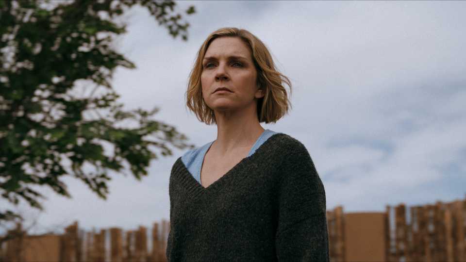 Rhea Seehorn olha seriamente pela janela em Pluribus