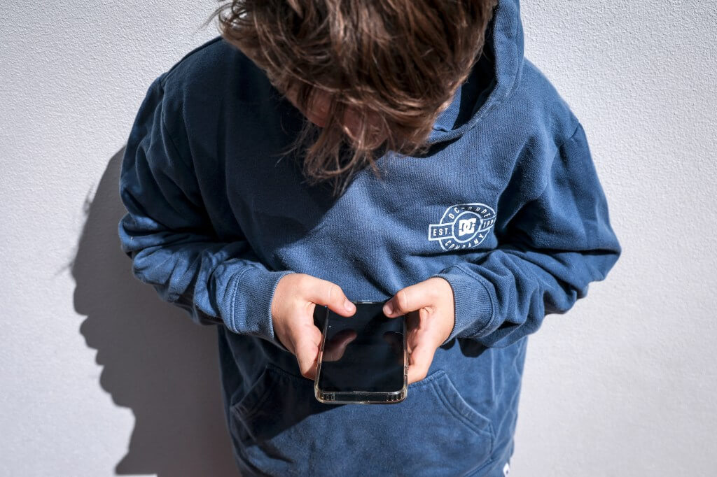 Países avançam para proibir redes sociais a crianças 1 Imagem de um adolescente olhando o celular; ilustrando o uso de redes sociais por menores.